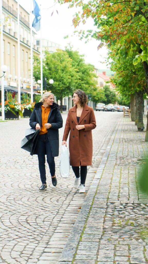 Två kvinnor promenerar längs en gata med gatsten i centrummiljö