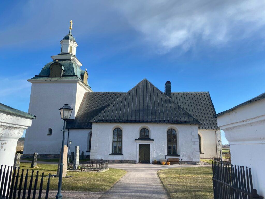 En exteriörbild på Tjällmo kyrka under blå himmel.