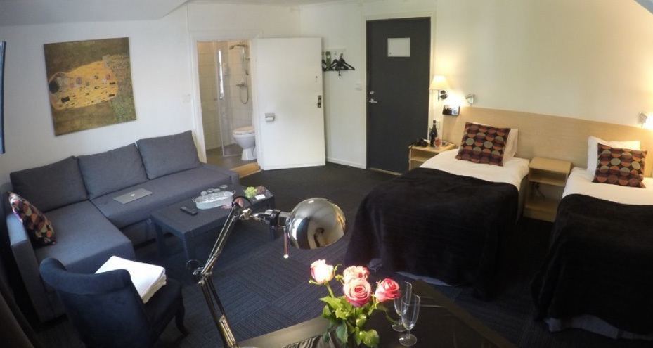 Hotellrum med dubbelsäng och soffa i grått.