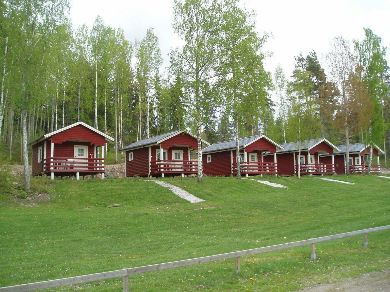 Röda campingstugor ligger på rad på en lite upphöjd gräsplan.