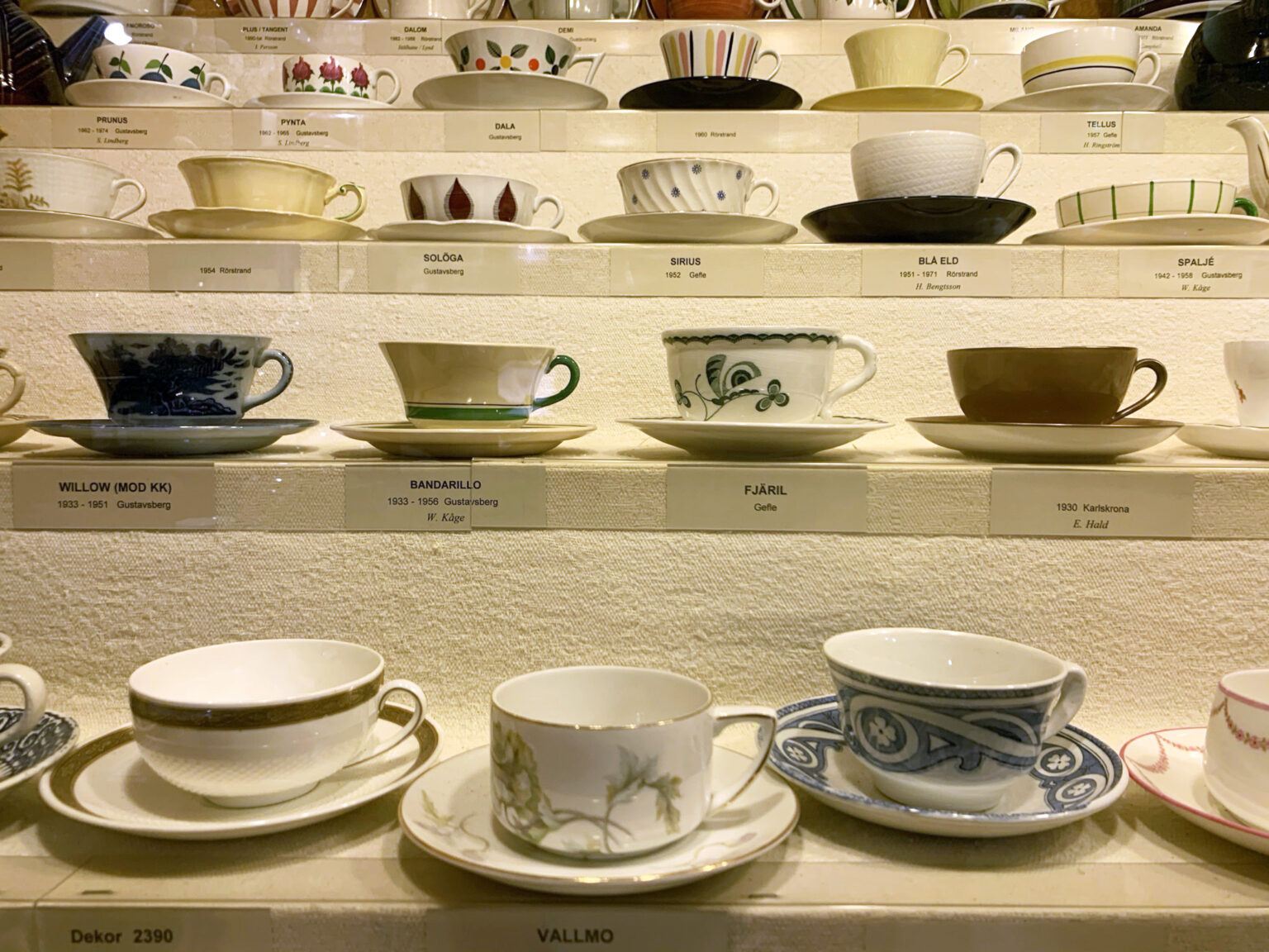 Flera hyllplan av olika kaffeserviser på ett svenskt porslinmuseum.