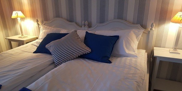 Hotellrum med säng. Detaljerna går i vitt och blått. Väggen har en tapet med vita och blå lodräta linjer.