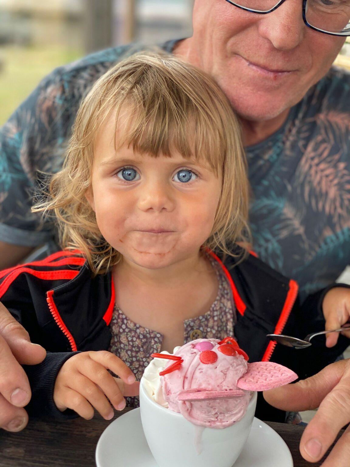 En liten tjej sitter i knät på en man och äter glass.