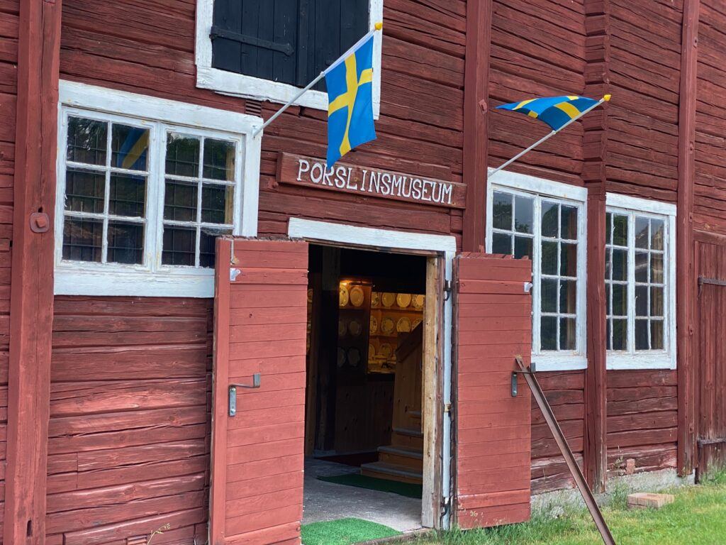 Exteriör av en röd träbyggnad med öppna dörrar. Ovanför dörren står det "Porslinsmuseum" på en dörr.