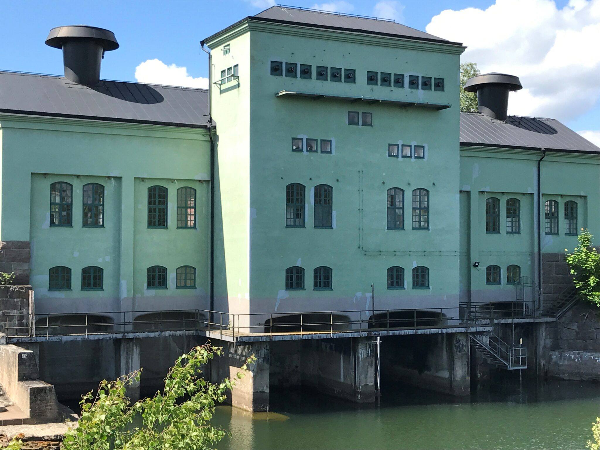 Stor gammal ljusgrön fabriksbyggnad som delvis är byggd i vatten.