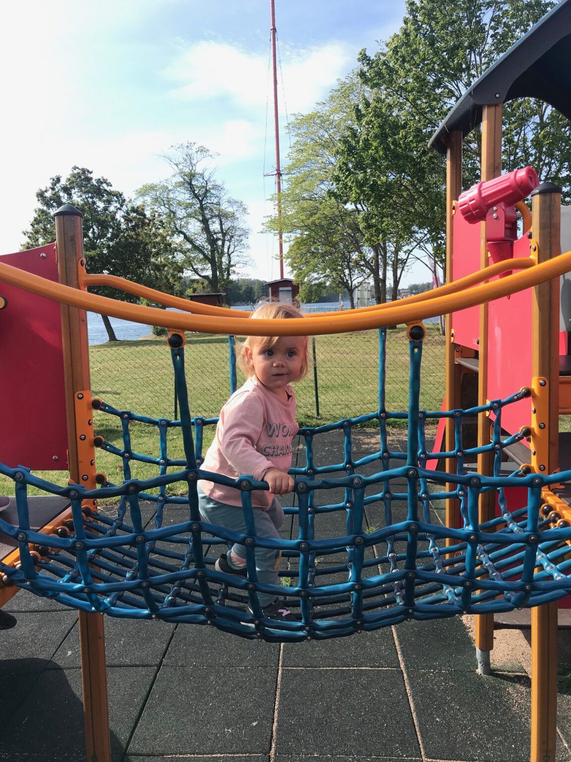 En liten tjej går över en nätbro i en lekpark.
