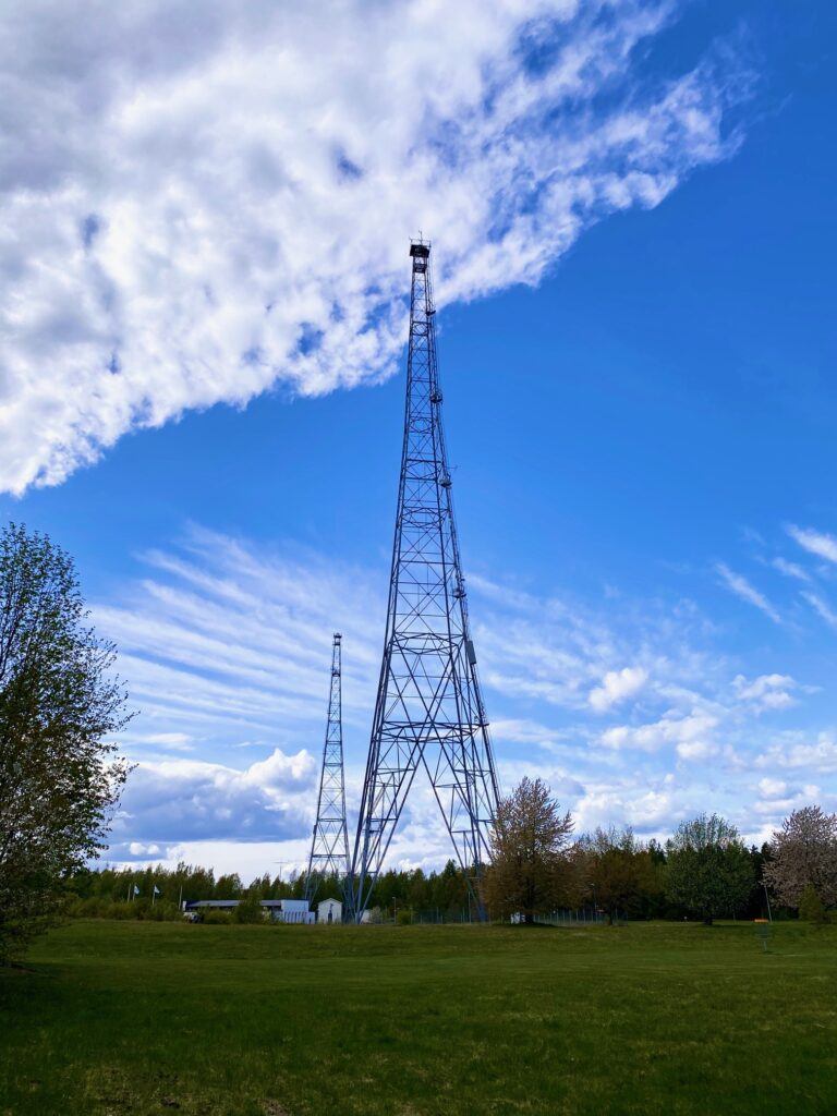 Två stora radiomaster reser sig över marken mot en blå himmel.