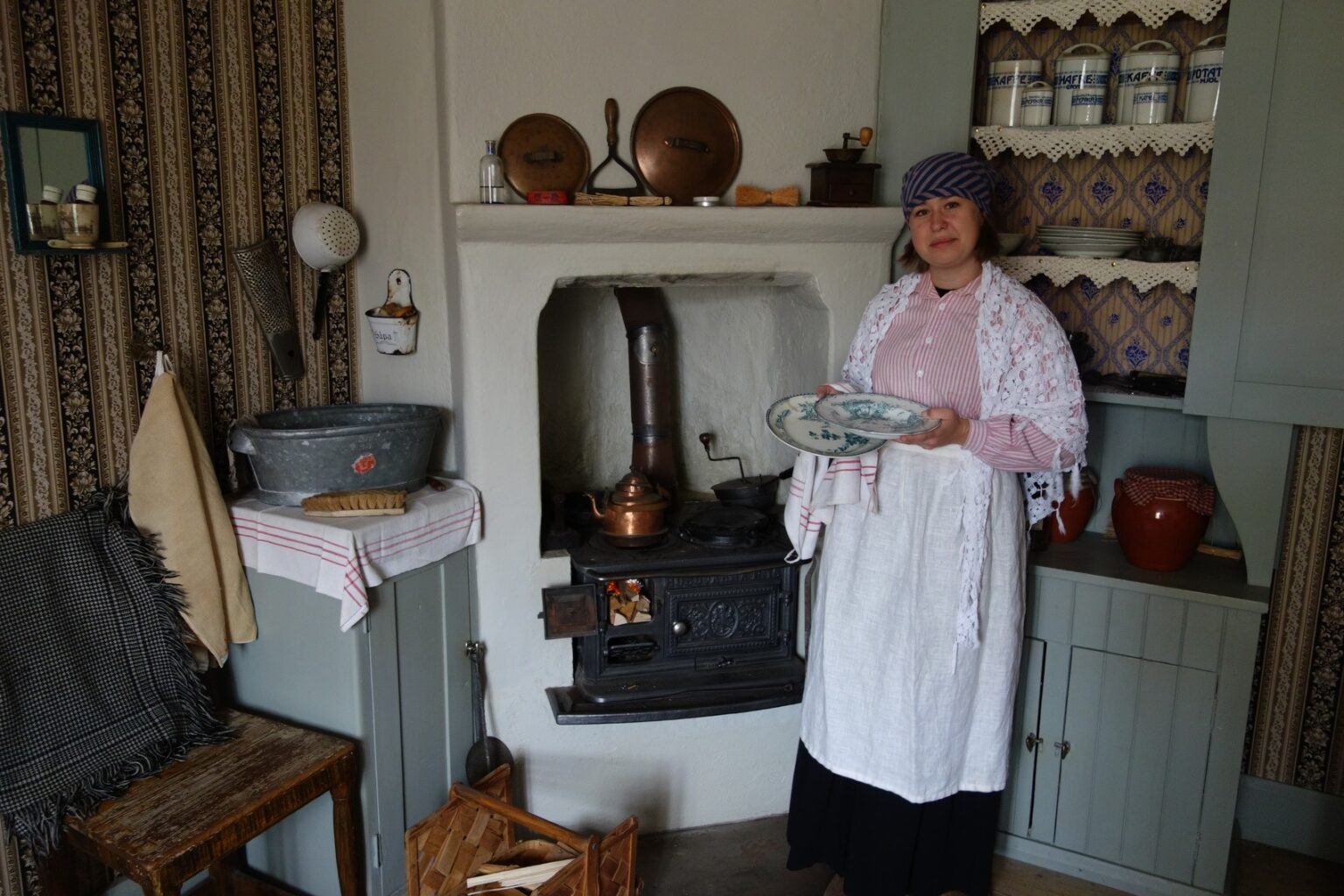 En kvinna klädd i tidsenliga kläder för 1800-talet står i ett gammalt kök.