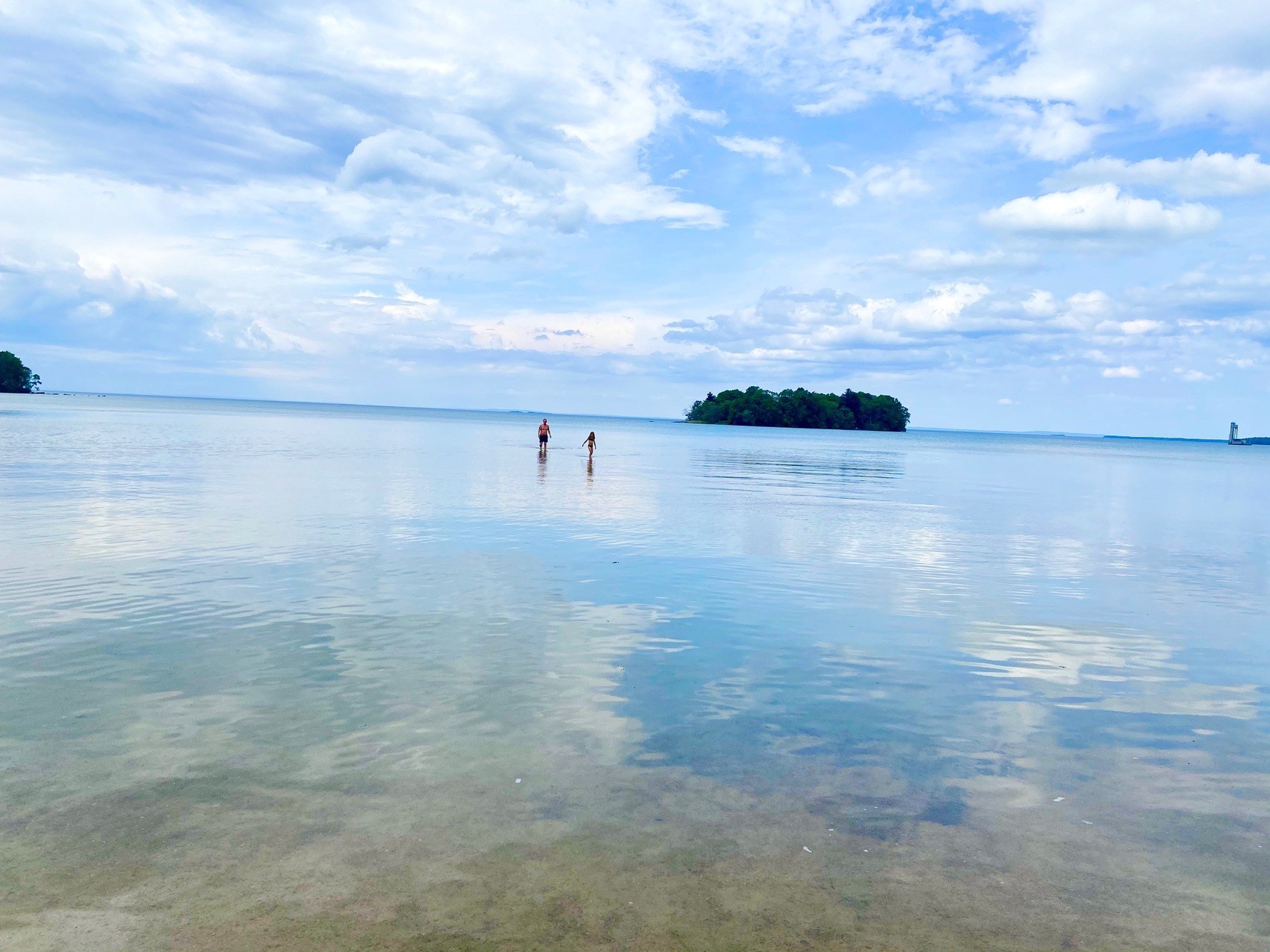 En bild på två personer som badar långt ut från stranden. I vattnet reflekteras himlen.