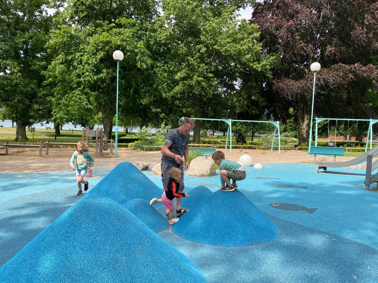 En man leker med några barn i en lekpark.