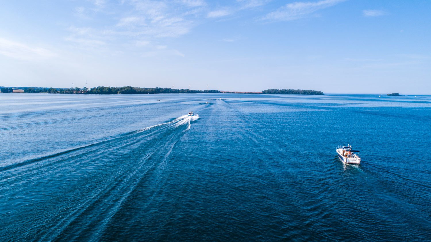 Drönarfoto över klarblått vatten och himmel. I vattnet åker två motorbåtar.