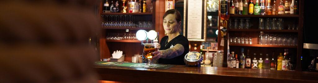Kvinna tappar öl i en mörk barmiljö.