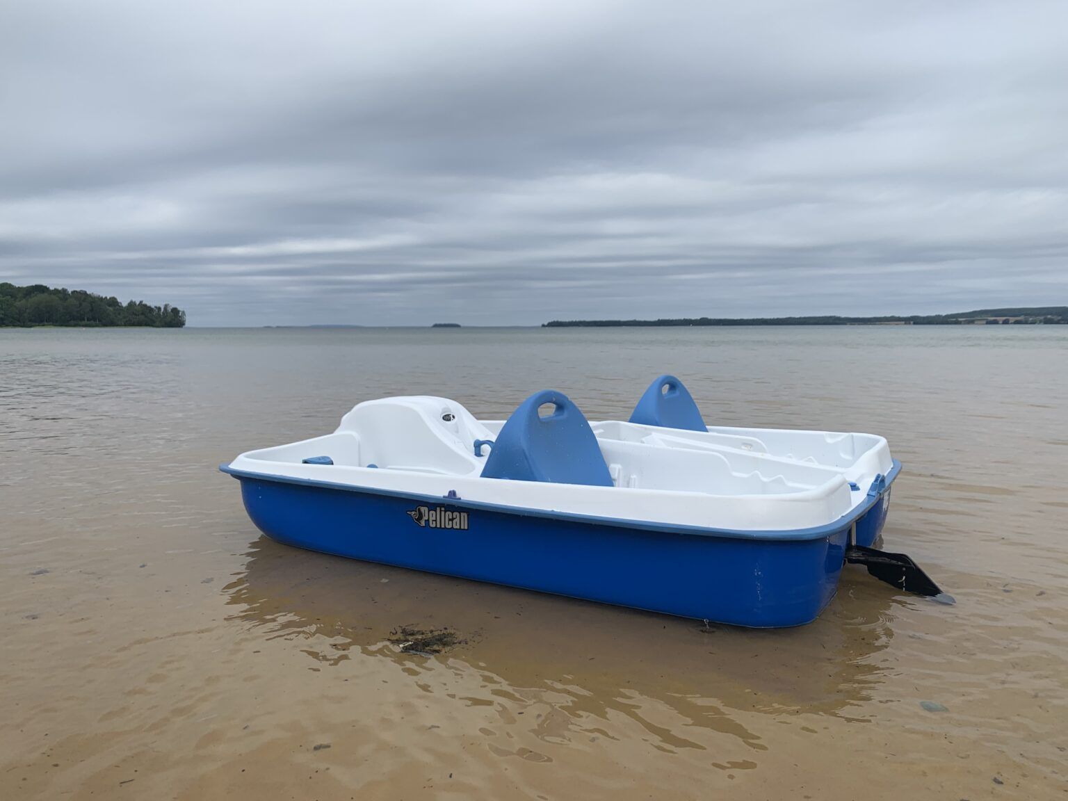 En blåvit trampbåt flyter på grunt vatten i Varamon.