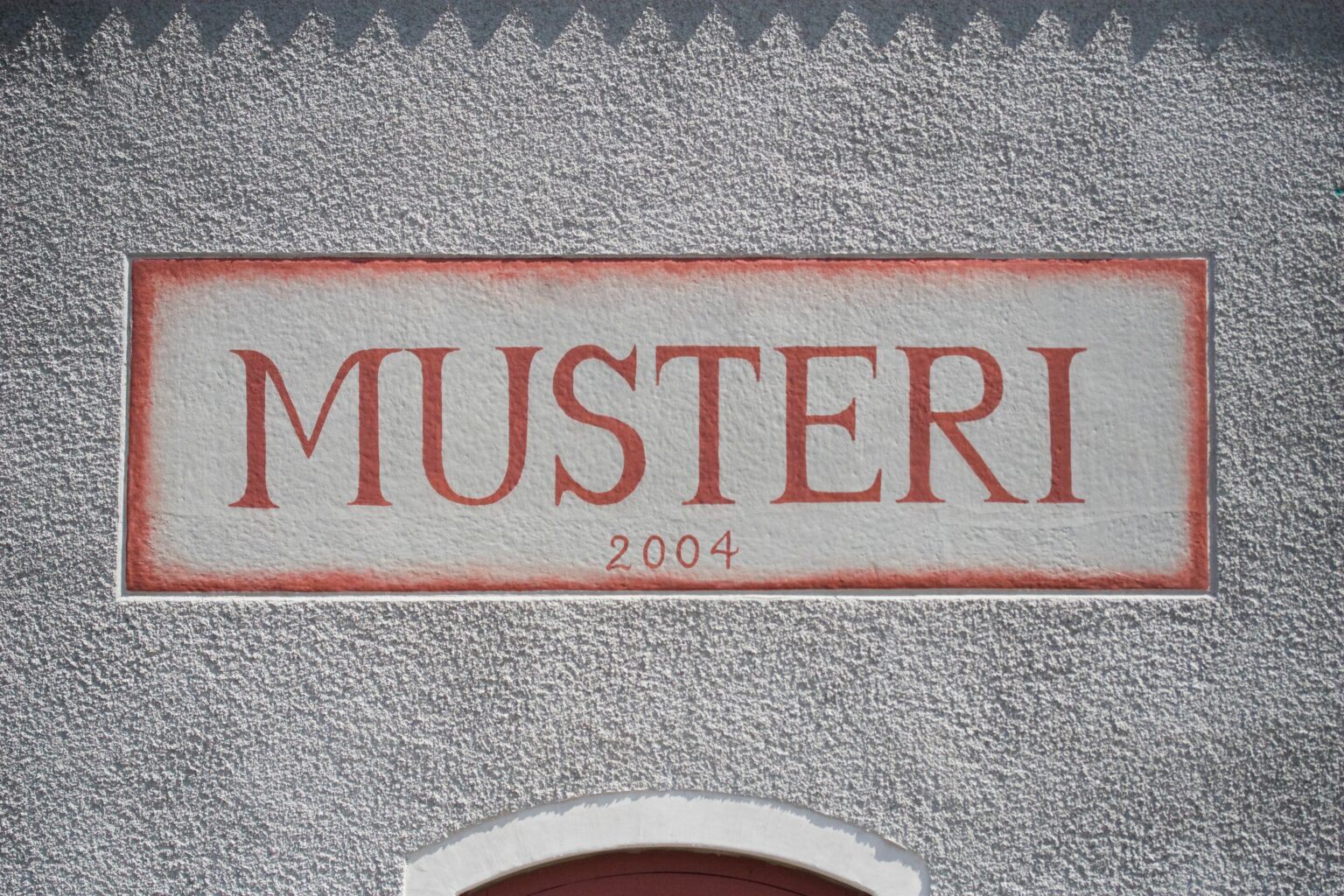 En bild på en vit stenvägg. På väggen står det "Musteri" med röd färg.