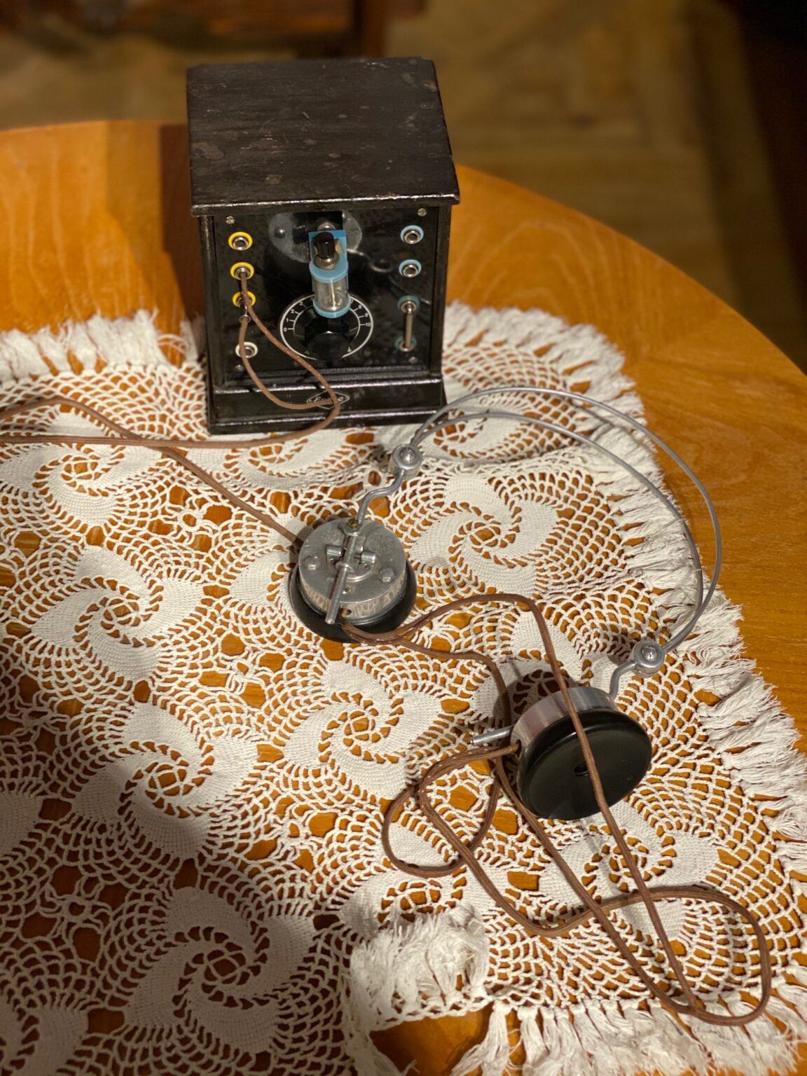 En mycket gammal telefon står på ett träbord med luren liggande på en brunvitfärgad duk.