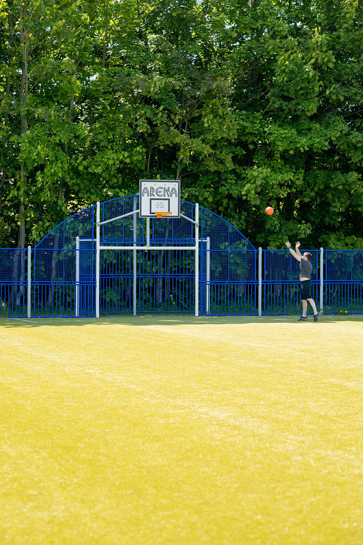 En man kastar basketboll mot en korg på en inhängnad konstgräsplan.