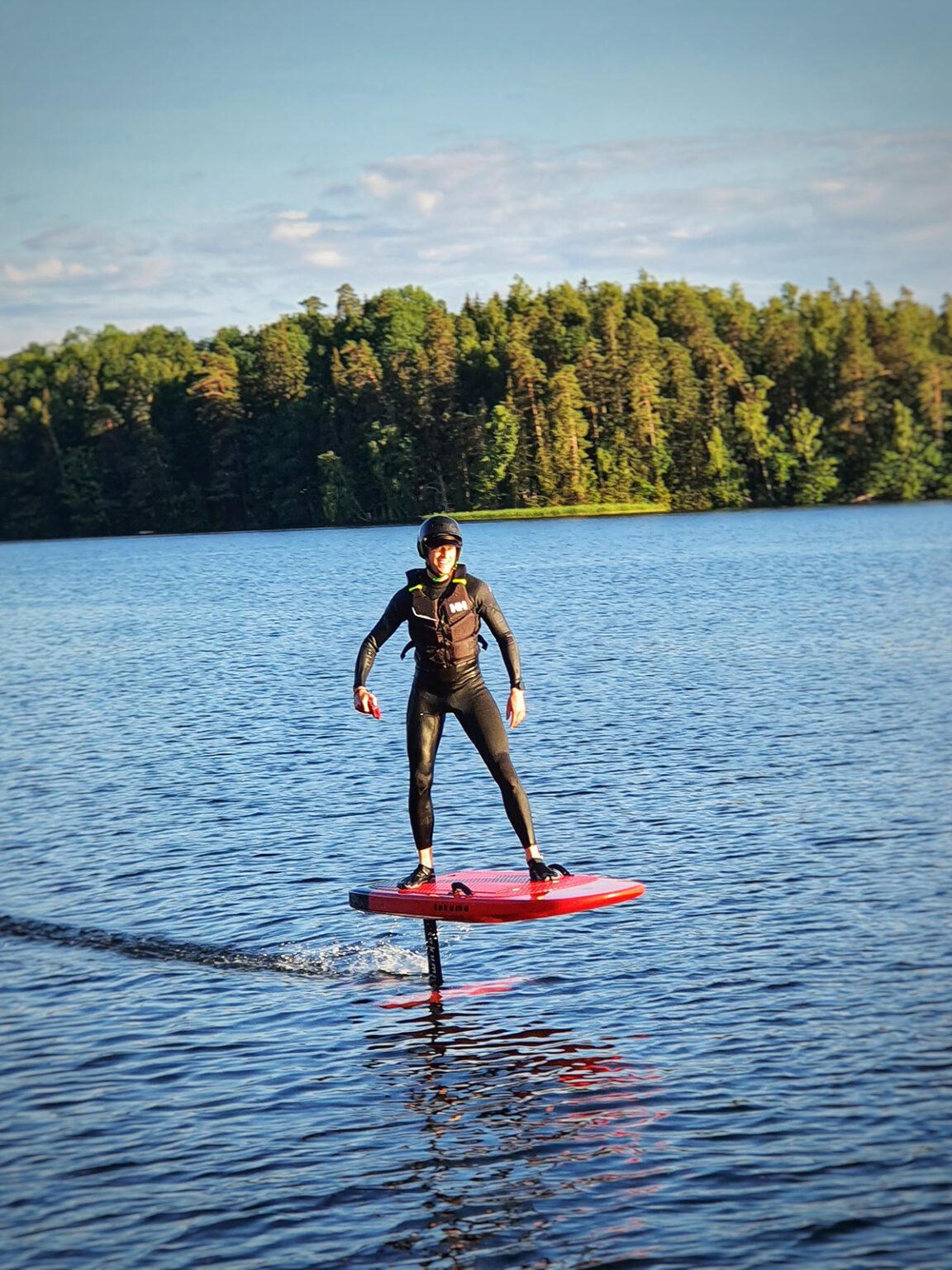 En man klädd i våtdräkt surfar på en bräda som är en halvmeter ovanför vattnet