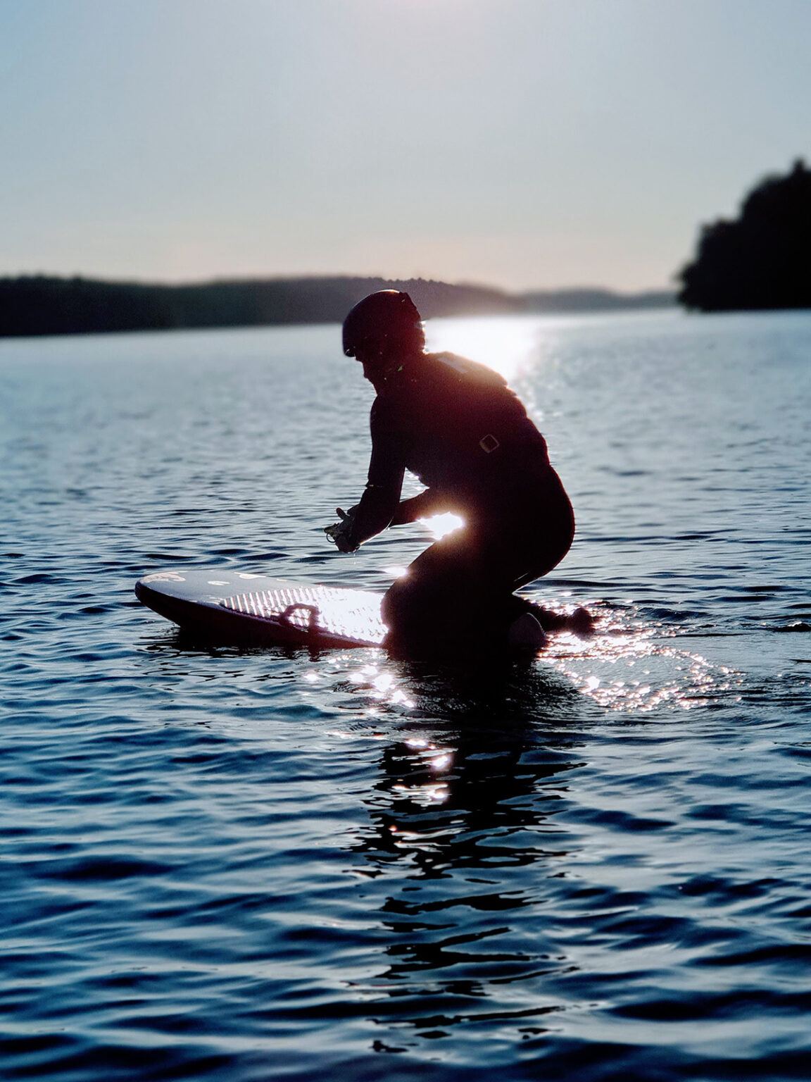 En surfare i sitter på sin bräda i vattnet, iklädd flytväst och hjälm.
