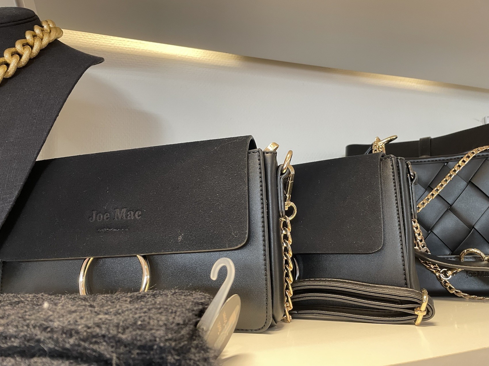 Svarta handväskor med guldkedjor står på en butikshylla.