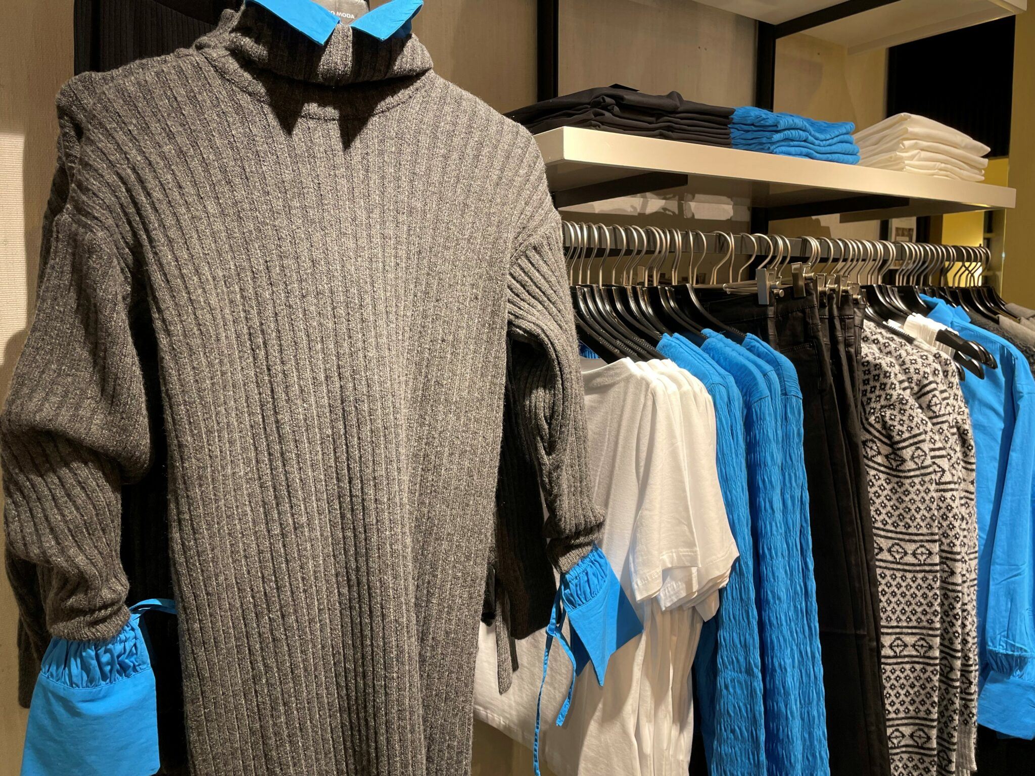 Kläder i blått och grått hänger i en klädaffär.