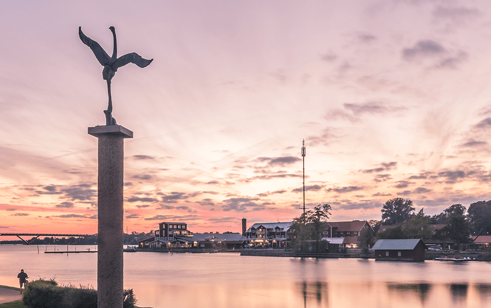 Vybild över Motala hamn under solnedgång. Åt vänster i bild står statyn tranan.