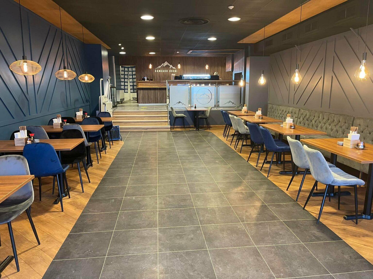 Interiörbild av sushirestaurang. Längs väggarna står blåa och gråa stolar.