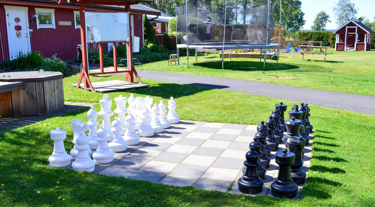 Ett stort schack står utanför en röd byggnad på campingen - Caravan Club Borensberg.