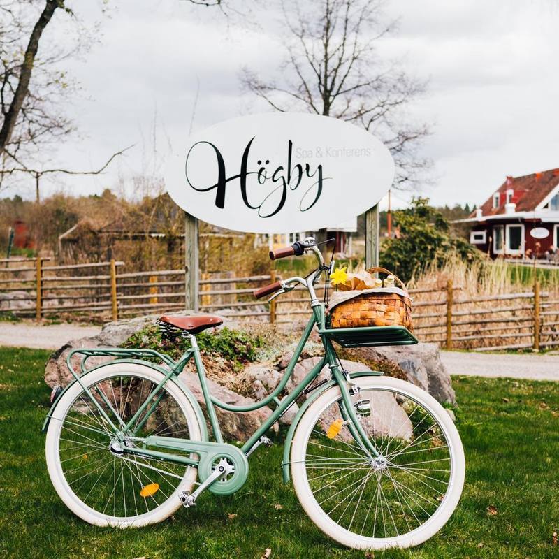 En grön cykel med vita däck står utomhus under en rund skylt där det står: "Högby Spa & Konferens"