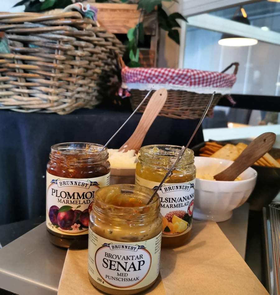 På en träbricka står flera glasburkar med senap och marmelad.