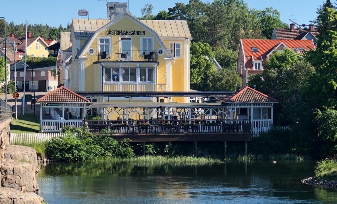 En bild på den gula Gästgivaregården i Borensberg, framför ses Motala Ström.