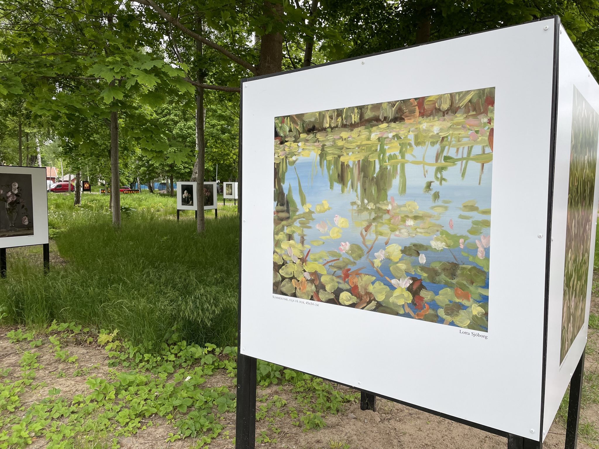 På de vita triangelformade skärmarna i Ringenparken syns olika typer av motiv från olika konstnärer. På skärmen i blickfånget ses en oljemålning över näckrosblad i en sjö.