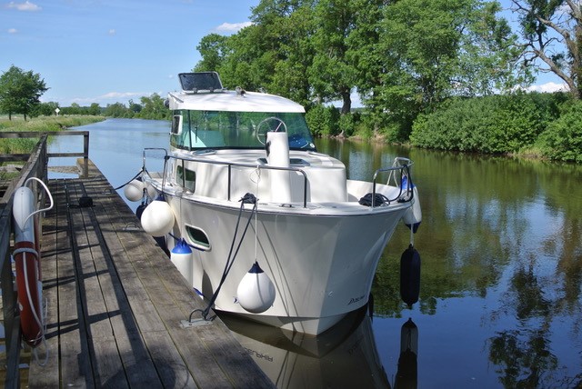 En vit charterbåt ligger förankrad längs med en brygga i Göta kanal.