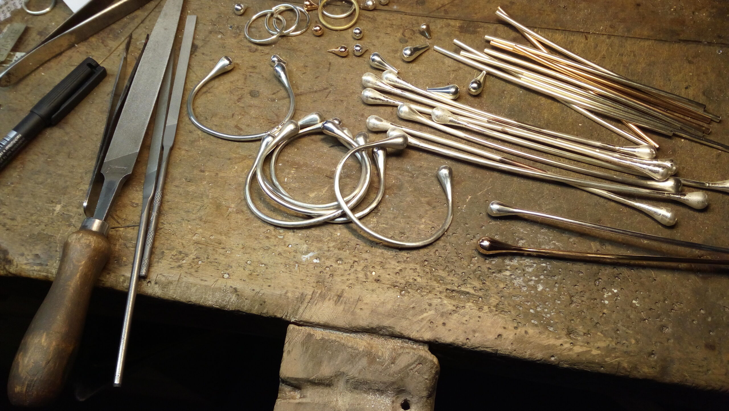 Ett arbetsbord för smyckestillverkning. På bordet ligger diverse verktyg och råmaterial för tillverkning.