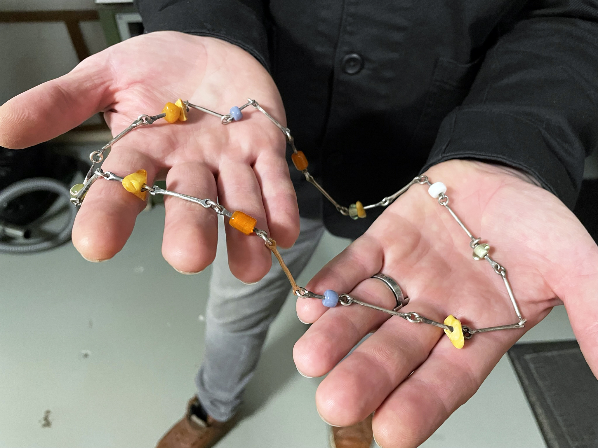 Händer håller i ett halsband med metallänkar och färggranna pärlliknande former.