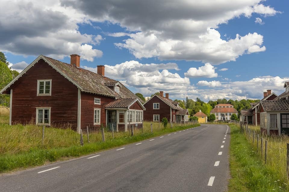 En asfaltsväg går mellan gamla, slitna röda hus med vita knutar.