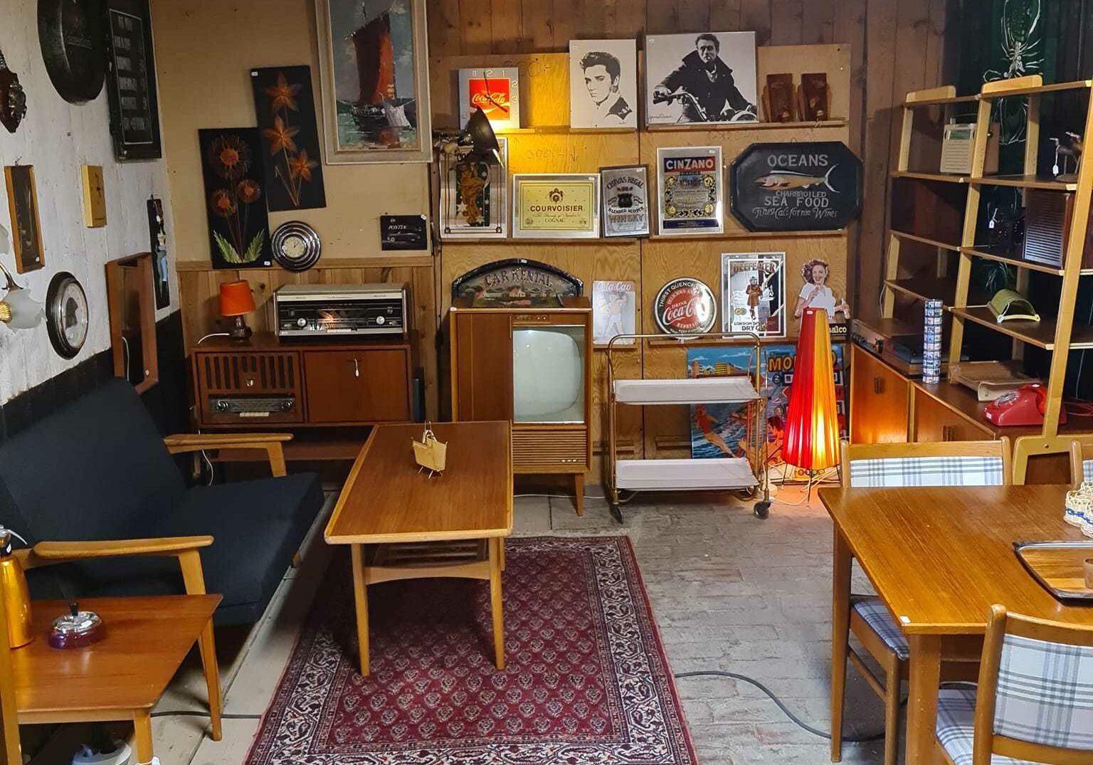 En interiörbild av Antikea nostalgistallet i Fornåsa. Gamla möbler från 60- och 70-talet pryder det möblerade rummet. På väggarna finns det tidsenliga tavlor och skivomslag.