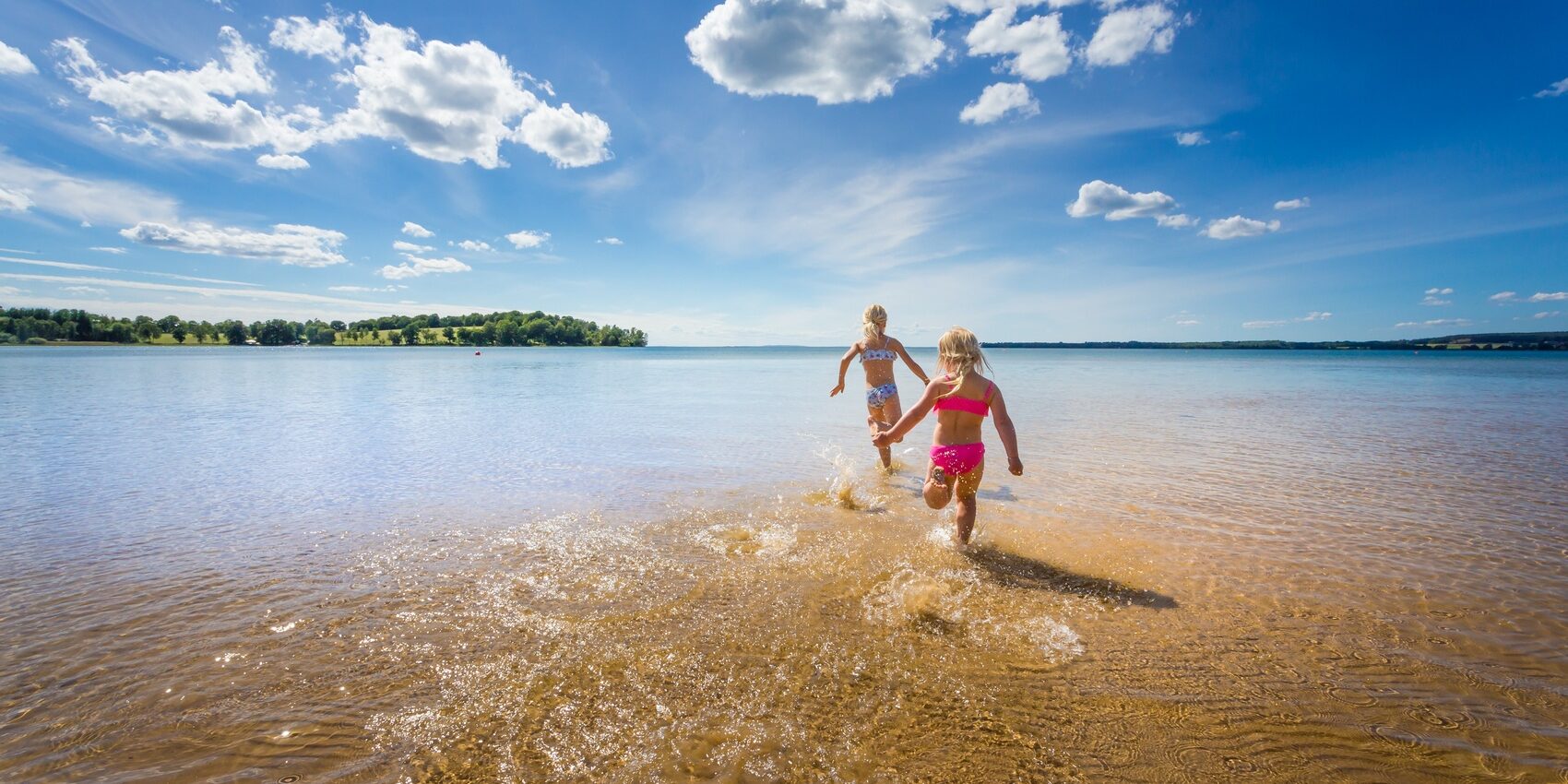 Två stycken barn springer ut i Varamons långgrunda vatten.
