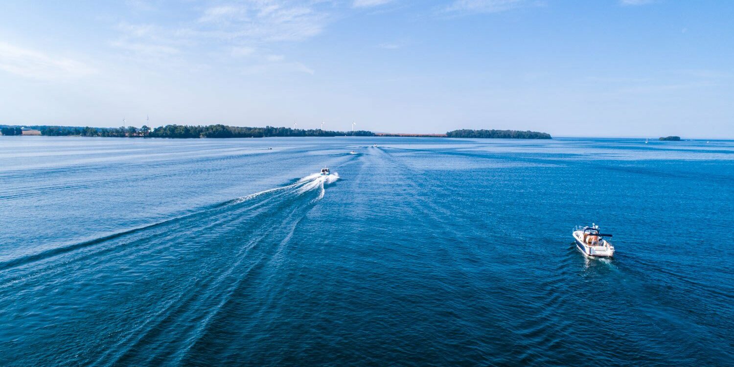 Drönarfoto över klarblått vatten och himmel. I vattnet åker två motorbåtar.